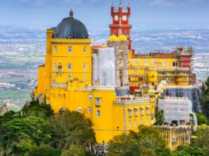 Beautiful, yellow, castle-like buildings sitting ontop of a forest hill.